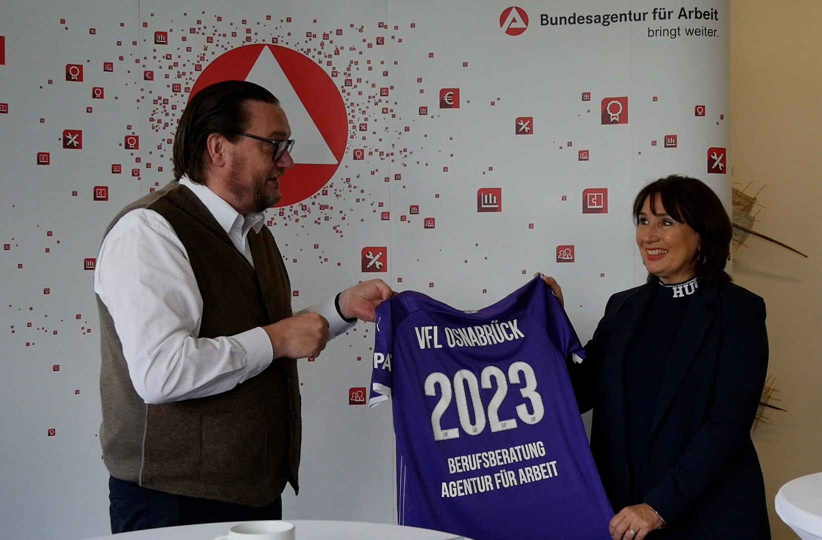 Dr. Michael Welling, Geschäftsführer des VFL Osnabrück und Christiane Fern, Leiterin der Osnabrücker Agentur für Arbeit halten gemeinsam ein VFL Trikot hoch